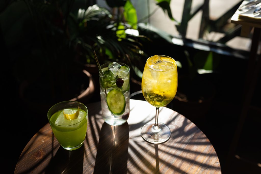 Three vibrant cocktails with citrus garnish on a wooden table, perfect for a summer drink setting.